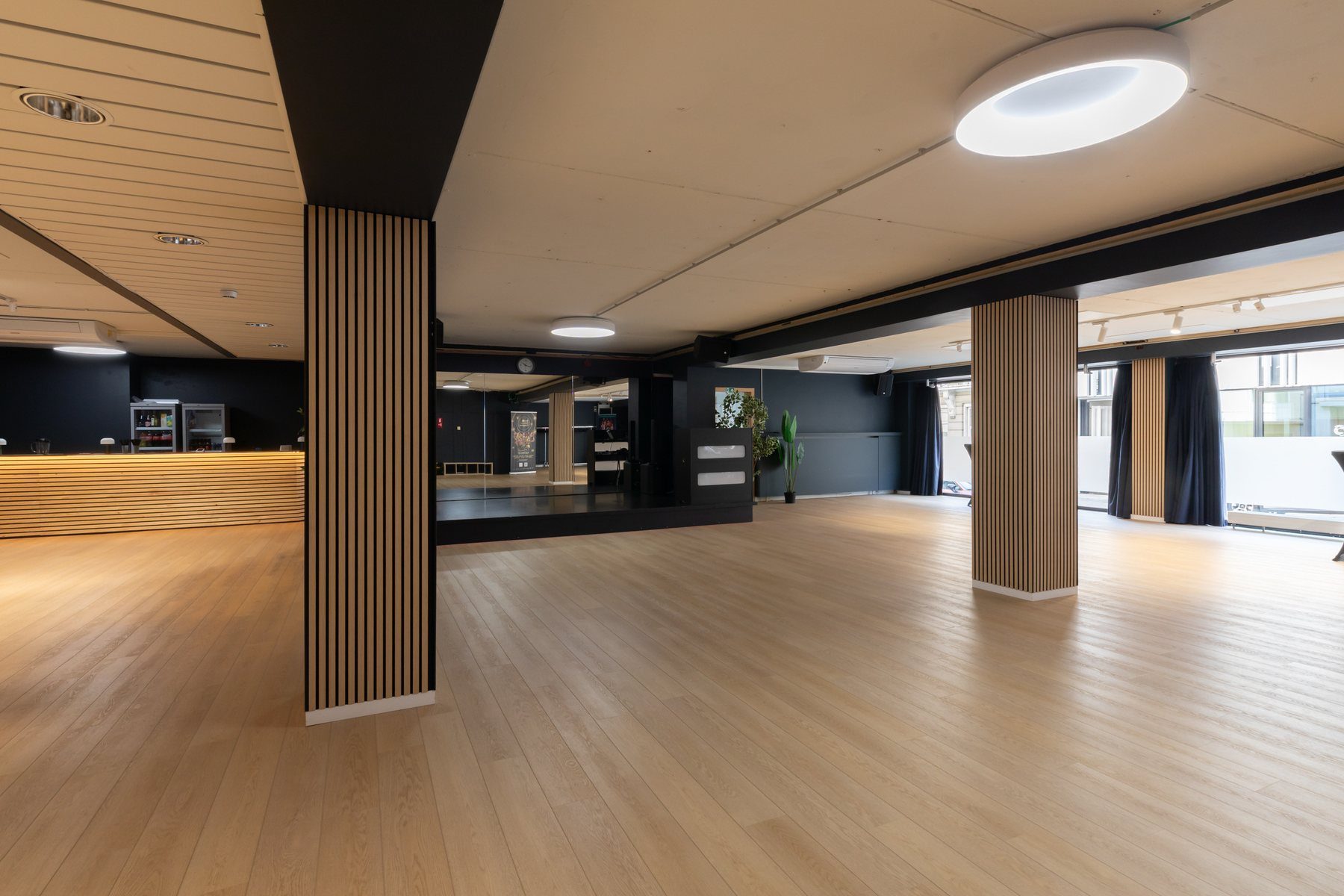The main room empty: pale oak floor, slatted columns, charcoal walls, wooden counter