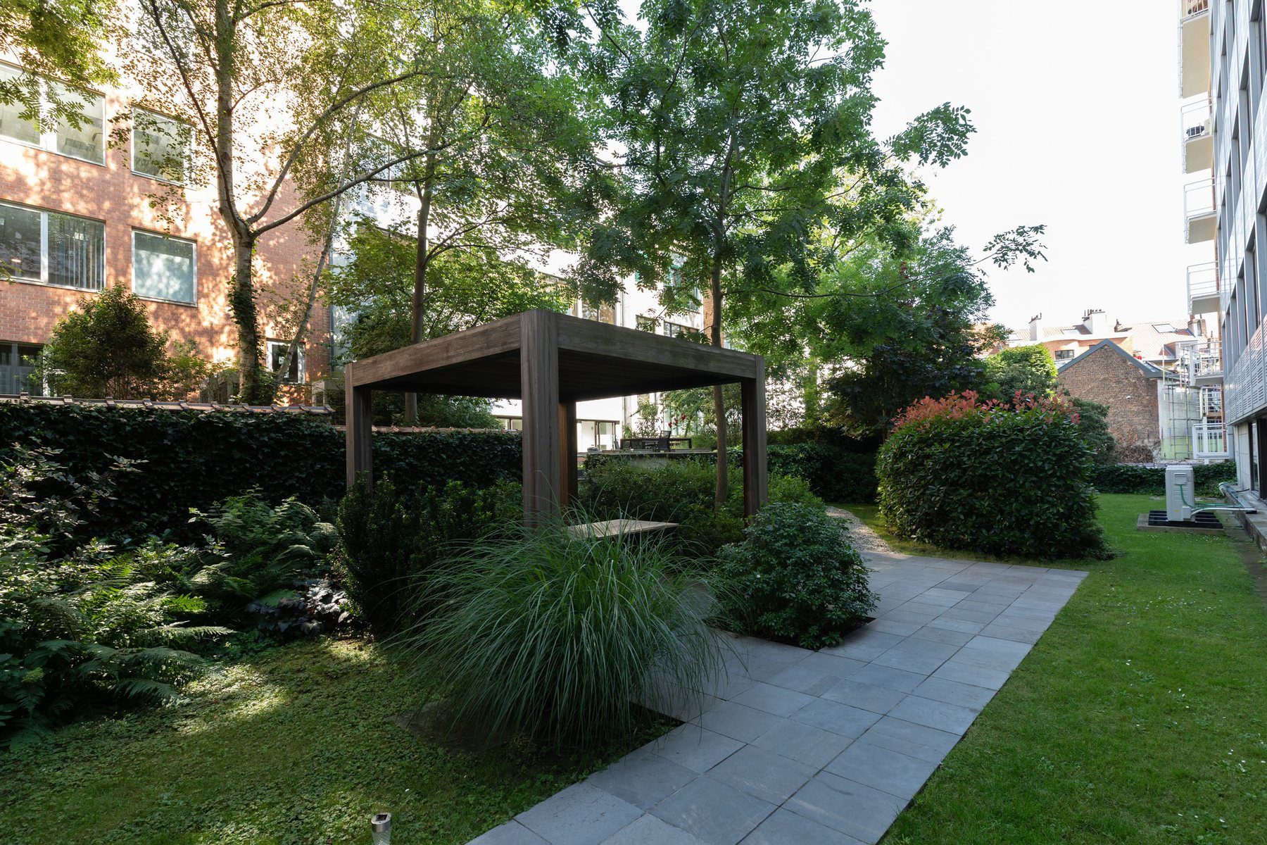 The inner garden at Studio 28: dark wooden pergola, blue cobbles, ferns, grasses and dense hedges