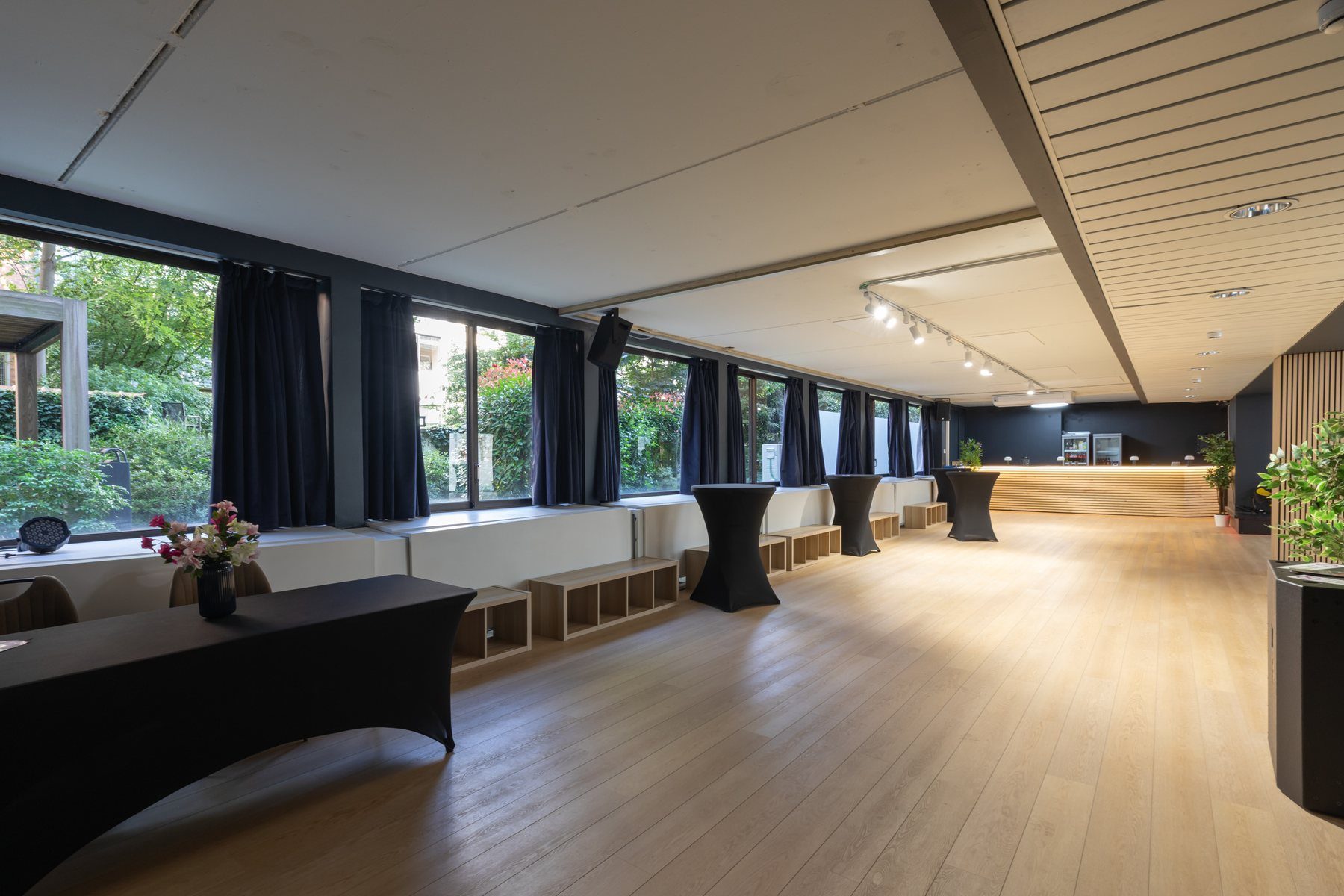 The main room at Studio 28: pale oak floor, dark walls, and the garden visible behind the glass doors
